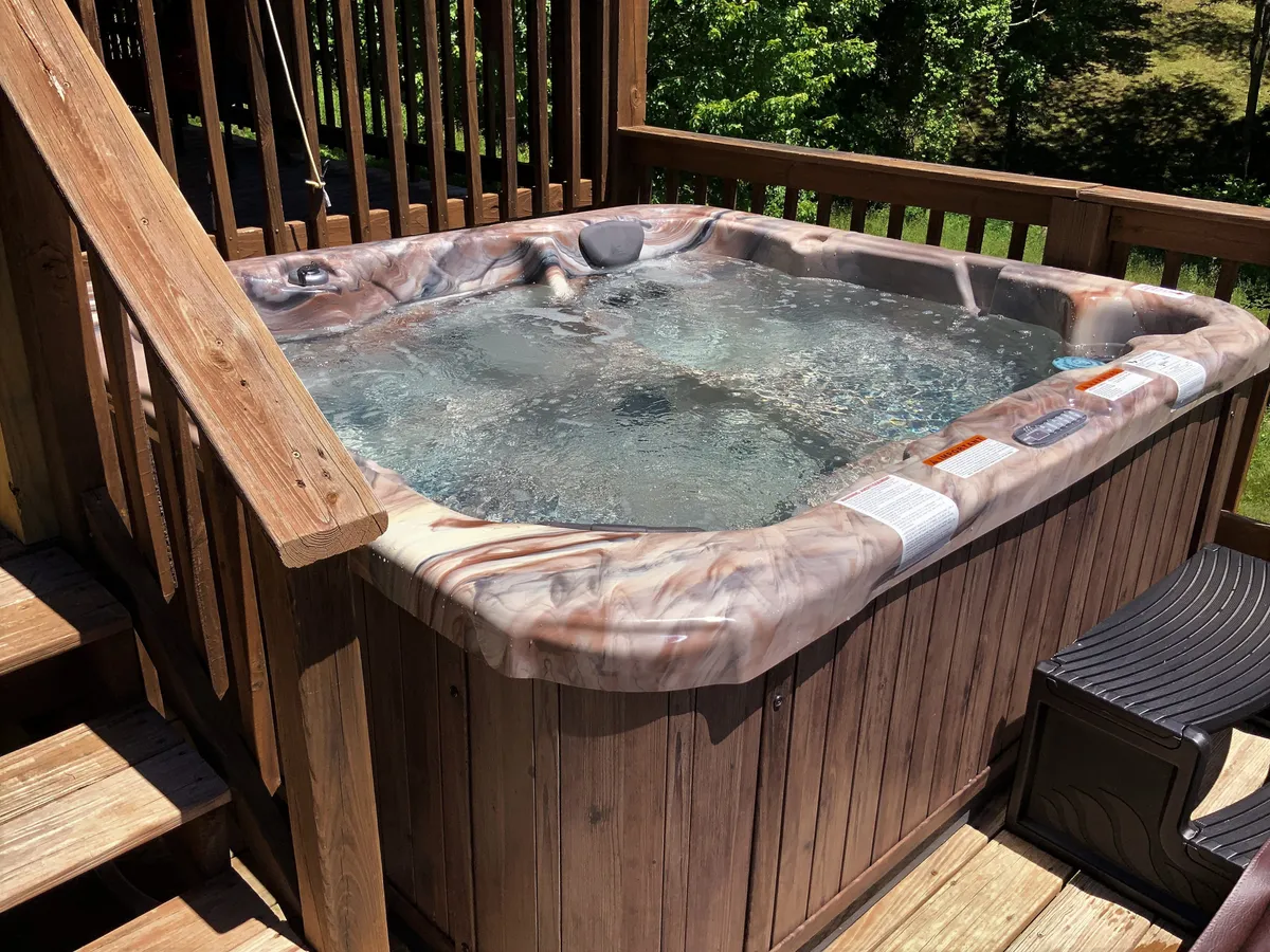 An inviting hot tub is set on a wooden deck, surrounded by lush greenery. The area looks private and tranquil, ideal for soaking muscles after a day of adventure. The deck is spacious enough for leisure and socializing, with natural views enhancing the sense of escape.
