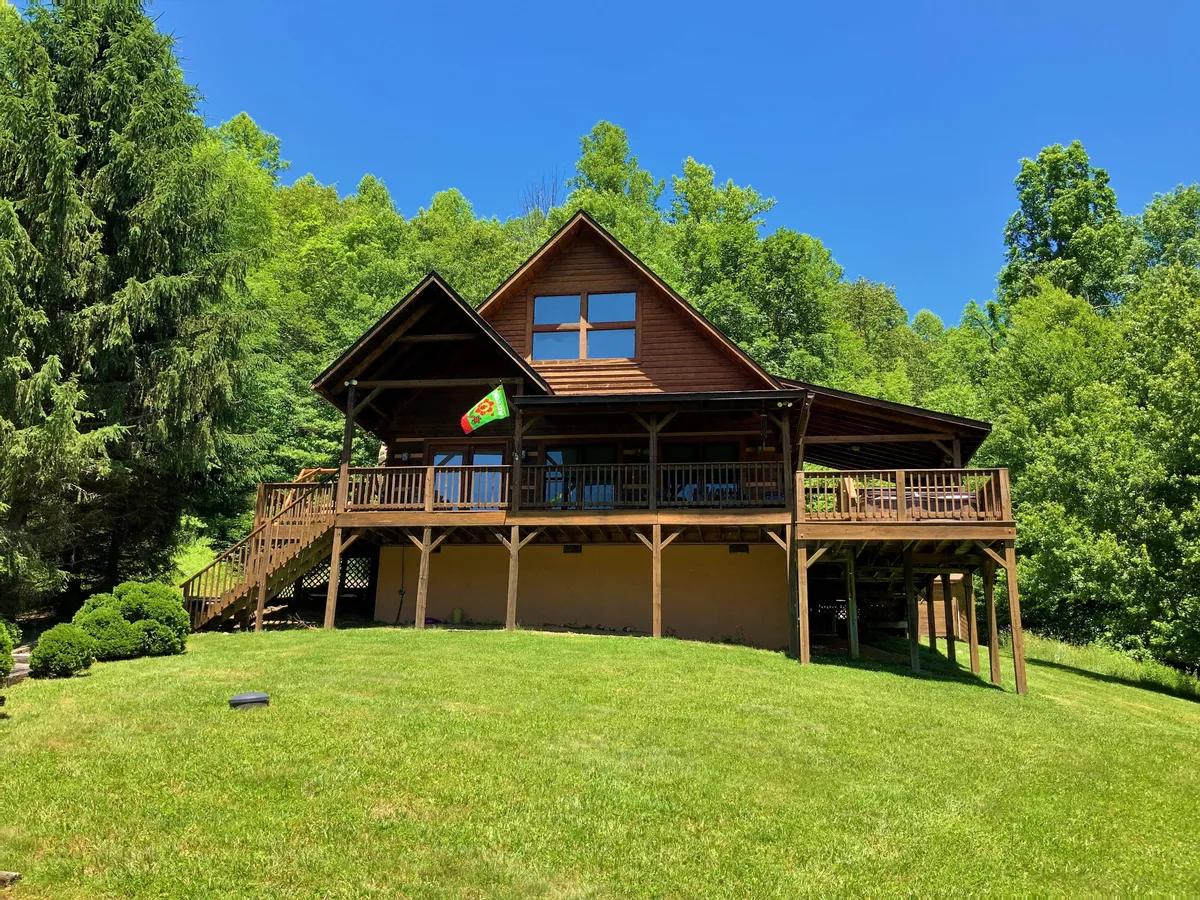 This image features the exterior of the property, showing a welcoming wooden deck with large windows that overlook a lush, green lawn. The scene suggests ample space for outdoor activities and relaxation, making it perfect for guests and their pets to enjoy the fresh air. A flag adds a touch of charm, and the expansive lawn hints at room for dogs to play or guests to embark on nature walks right from the doorstep.