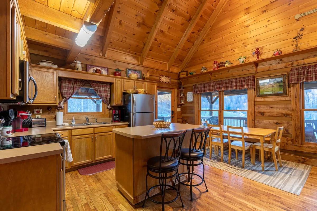 This image highlights the modern, well-stocked kitchen with a spacious island and bar stools, warm wooden cabinetry, and large windows framing a scenic view. The arrangement suggests a welcoming place for cooking, casual dining, and socializing, blending modern amenities with rustic charm.