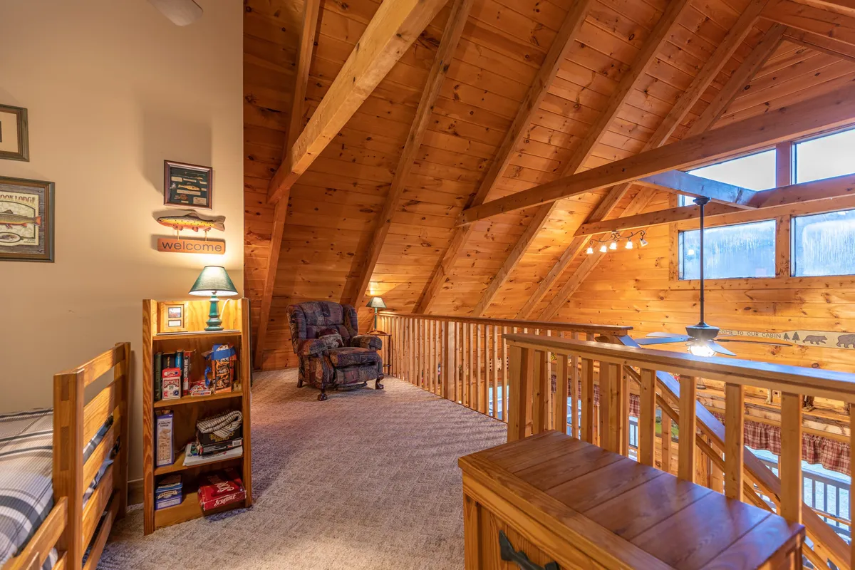An inviting interior scene featuring exposed wooden beams, large windows that frame scenic outdoor views, a comfortable chair, and a bookshelf. The layout encourages relaxation after a day outdoors, with the sunset visible through the windows reinforcing the connection between interior comfort and the surrounding natural beauty.