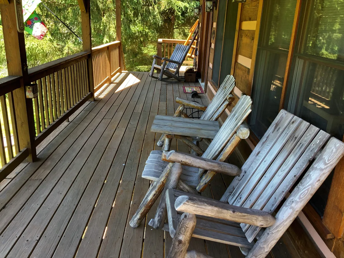 A spacious covered porch with classic wooden rocking chairs overlooking a lush green landscape. The tranquil setting is framed by natural greenery, inviting guests to relax and connect with nature. The porch is sheltered, making it a welcoming space for enjoying both sunrise coffee and evening stargazing.